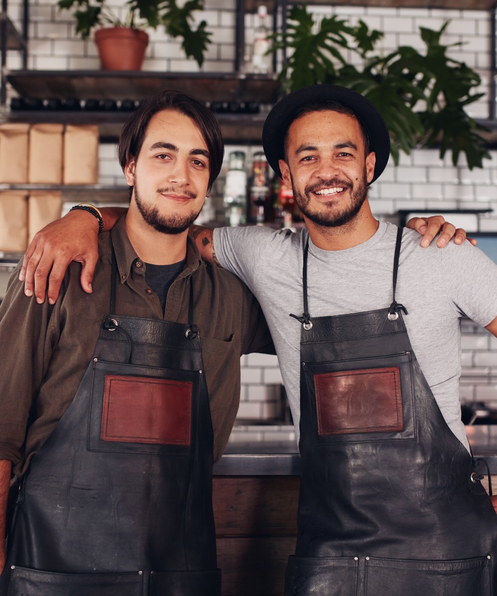 Zwei lächelnde Café-Mitarbeiter in Leder-Schürzen als Gesichter erfolgreicher regionaler SEO